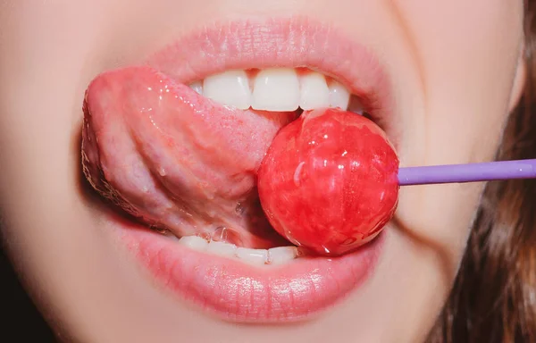 Szoros női ajkak rózsaszín szájfény tartja a szájban piros nyalóka cukorka. Nyalóka az arcon. — Stock Fotó