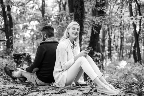 Coppia felice in passeggiata autunnale. Coppia d'affari - uomo che naviga Internet su un notebook, donna che usa il telefonino all'aperto. Business outdoor nel parco autunnale . — Foto Stock