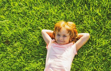 Çimlerin üzerinde yatan tatlı bir çocuk. Mutlu özgürlük çocuğu sahada eğleniyor ve hayal kuruyor. Doğayla birlik.
