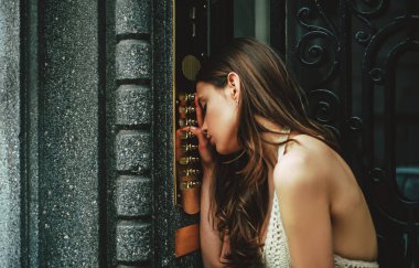 Bina girişinde bayan dahili telefon zili var. Genç elbiseli kadın kapı klavyesine kod giriyor..