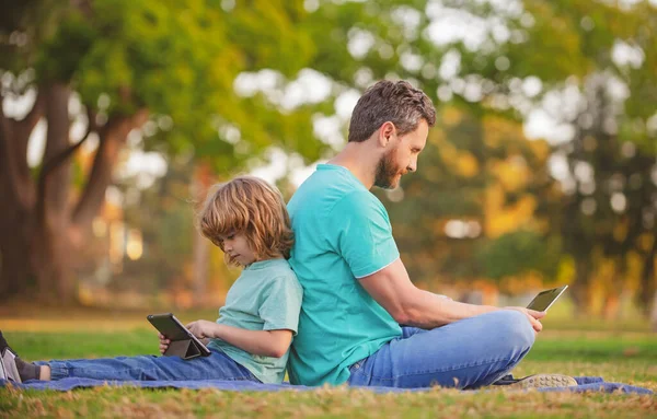 Kid with daddy learning lesson. Father and son use laptop, dad and school boy child looking tablet. Outdoor distance learning. — Stock Photo, Image