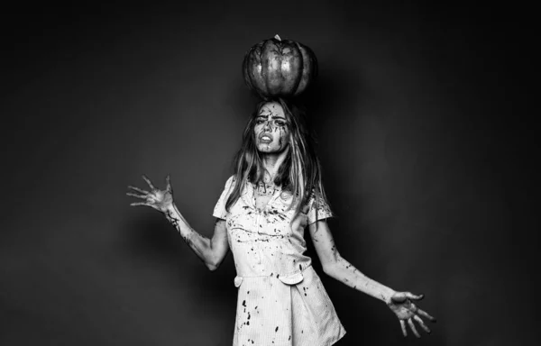 Jolie jeune femme blonde vêtue de robe aux citrouilles. Sexy zombie fille tenant une citrouille au-dessus de sa tête. Modèle avec des mains ensanglantées et du sang sur le visage. Halloween maquillage belle femme . — Photo