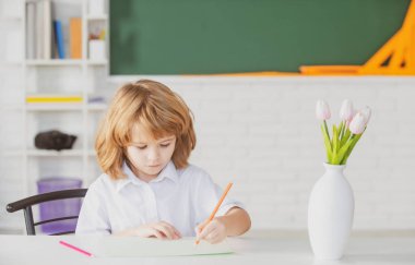 School kid writing in copybook and sitting at table in classroom. First grade.