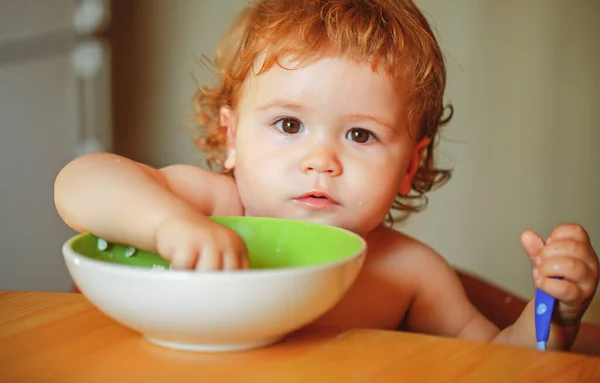 Portret zabawnego chłopczyka jedzącego z talerza trzymającego łyżkę zbliżenie. — Zdjęcie stockowe