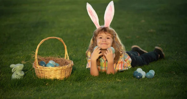 Child boy hunting easter eggs in spring lawn laying on grass. Bunny kids with rabbit bunny ears. — Stock Photo, Image