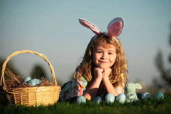 Easter egg hunt in garden. Child boy playing in field, hunting easter eggs, on sky background with copy space. Closeup portrait of cute kids. — стоковое фото