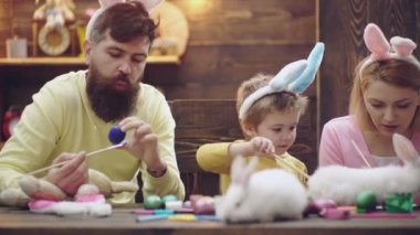 Happy family of mother, father and child son drawing easter eggs at home, painted eggs. Family celebrating easter with kids at home. Spring family holidays. Funny cute kids face.