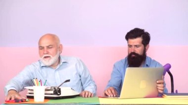 Yaşlı ve Genç. Yetişkin oğul, yaşlı babaya bilgisayarda yardım ediyor. Parlak ofis alanında dizüstü bilgisayar kullanan iş adamları.