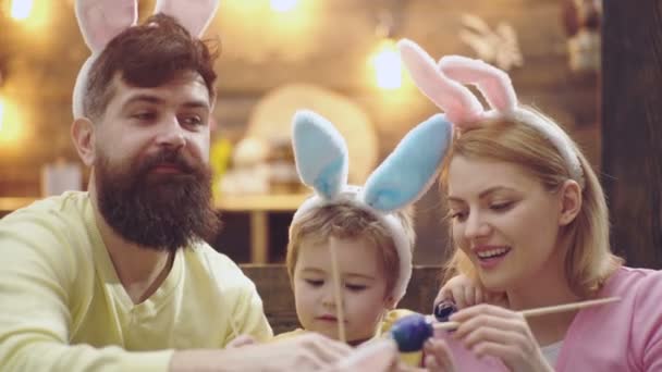 Szczęśliwa rodzina matki, ojca i syna rysujących wielkanocne jajka w domu, malowane jajka. Rodzina świętująca Wielkanoc z dziećmi w domu, śmieszne króliki wielkanocne rodzice z dziećmi w króliczych uszach. — Wideo stockowe