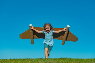 Child boy playing with cardboard toy airplane wings craft in sky with copy space for text. Creative with family and dreaming of flying concept. Travel and imagination concept.