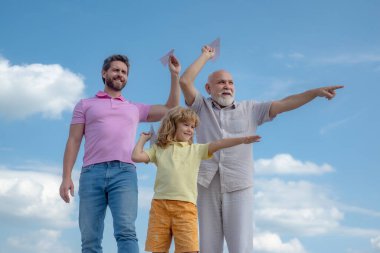 Men generation: grandfather father son and grandson playing with toy paper plane outdoor on sky. Boy dreams of becoming a pilot.
