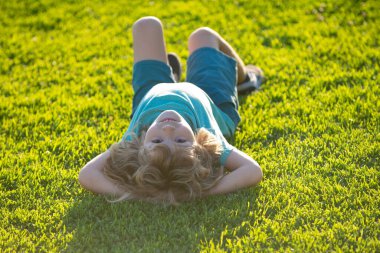 Happy child laying upside down on green grass in summer Park. The concept of a healthy lifestyle. The fun and carefree childhood.