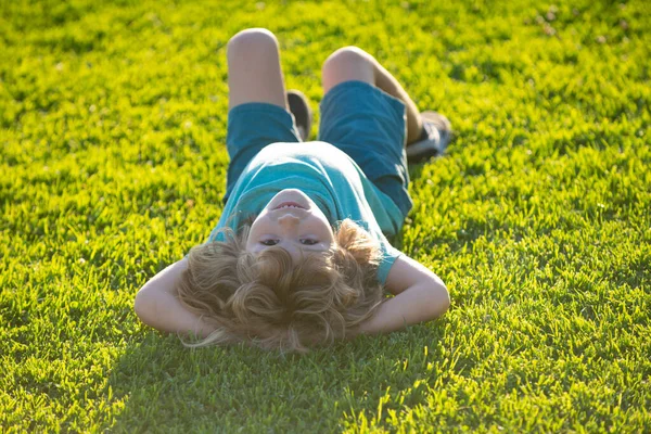 Щаслива дитина лежить догори ногами на зеленій траві в літньому парку. Концепція здорового способу життя. Веселе і безтурботне дитинство . — стокове фото