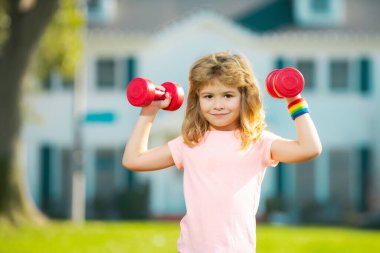 Sport exercise for kids. Sporty children, healthy Lifestyle. Child boy lifting dumbbells outside. Funny excited child sportsman.