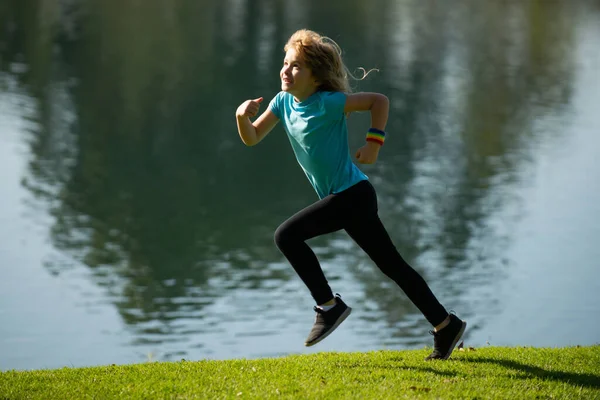 Kids running or jogging near lake on grass in park. Boys runner jogging in outdoor park. Running is a sport that strengthens the body. Kids running on green meadow against sea or lake. — Stock fotografie