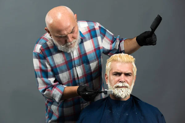 Bearded man coloring hair. Hair salon, hair coloring man. Attractive senior barber doing a haircut and haircolor for client at barber shop. Hipster guy dye his hair color on a gray background. — Stok fotoğraf