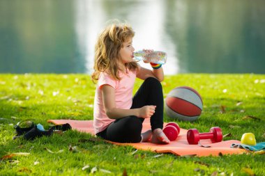Child boy drink water relax on sport mat after sport exercises outdoor in park. Concept of children sport.