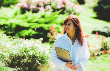 Laptop bilgisayarı olan kızıl saçlı bir kız öğrenci. Bahar Güzel, kızıl, dantel elbiseli, çiçek açan bahçede duran romantik kız..