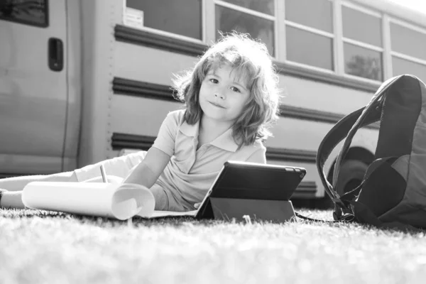 Schlauer Schuljunge bei Hausaufgaben mit digitalem Tablet im Schulpark in der Nähe des Schulbusses. Kind nutzt Geräte zum Lernen im Freien. — Stockfoto