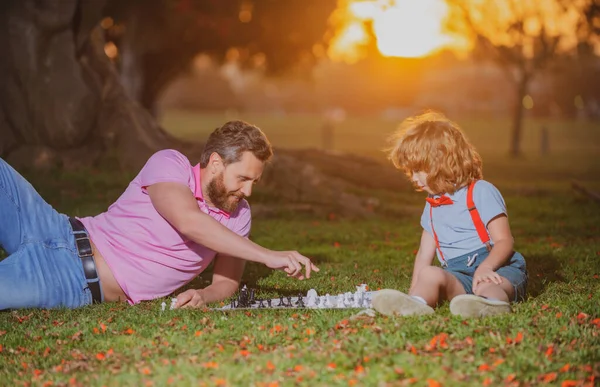 Ojciec i syn grający w szachy leżący na trawie w parku trawników. Dzień Ojca, rodzina miłości, rodzicielstwo, koncepcja dzieciństwa. Aktywni ludzie bawią się i grają w szachy w parku, spędzają czas z dzieckiem. — Zdjęcie stockowe