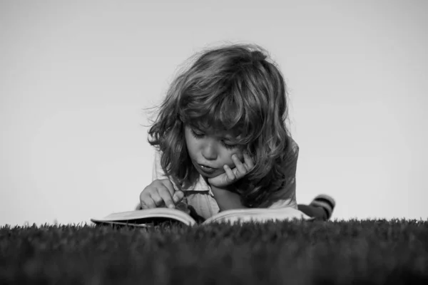 O rapaz está a ler um livro no parque primaveril. Relaxar na relva do jardim. Educação ao ar livre. Crianças imaginação, inspiração crianças. — Fotografia de Stock