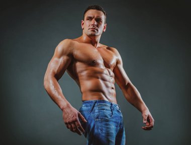 Portre yakışıklı seksi kaslı adam, mükemmel vücutlu, esmer arka planda bir atlet. Gri stüdyodaki seksi kaslı güçlü yüzlü adam izole edilmiş..