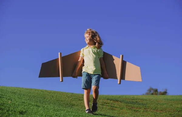 子供が飛ぶ。青い空におもちゃの段ボール飛行機の翼で飛ぶ面白い子の少年パイロット、コピースペース。自由の概念を始めろ屈託のない子供. — ストック写真