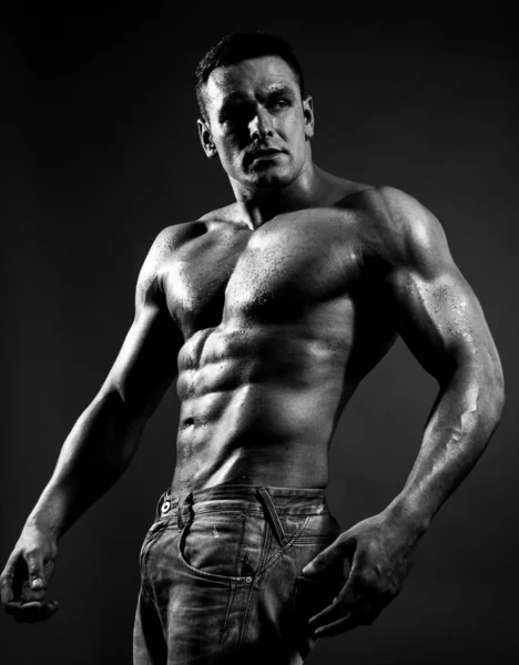 Sexy caucasian man in jeans standing with naked torso, guy showing six-pack abdominal abs, have perfect body, dark black background. — стоковое фото