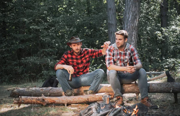 Ungdomar njuter av picknick i parken på sommardagen och dricker öl. Turismbegreppet. Picknickvänner. Två vänner skogsarbetare sitter i skogen och dricker öl. — Stockfoto