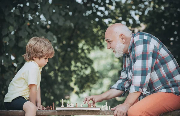 Un niño jugando al ajedrez con su abuelo. Pieza de ajedrez. Hombre mayor pensando en su próximo movimiento en una partida de ajedrez. Abuelo jugando ajedrez con su nieto . — Foto de Stock