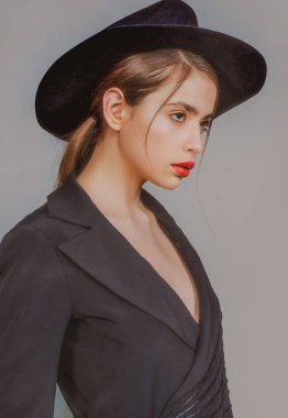 Moda şapkalı genç kadın. Güzel kız portresi. Moda şapkalı, kırmızı dudak makyajlı şık bir kadın. Moda görünüşü, güzellik ve tarz. Gri arkaplan.