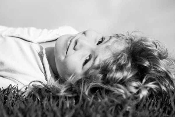 Portrait of a smiling little boy lying on green grass and dreaming. Cute child enjoying nature outdoors. Healthy carefree kid playing outside in summer park on a lawn. — Stock Photo, Image