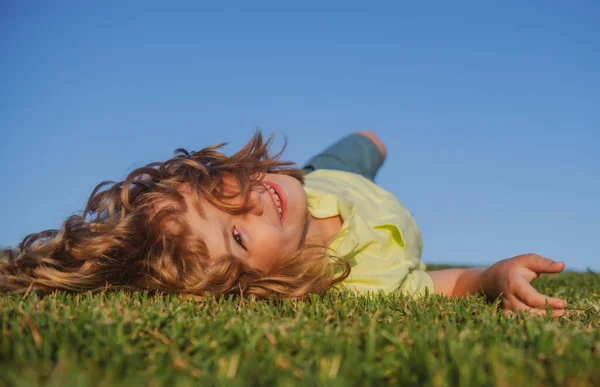 Grabben låg på det gröna gräset. Glada barn leker i gröna våren fält mot himlen bakgrund. Frihet barn och fantasi koncept. — Stockfoto