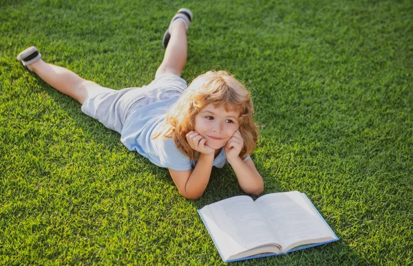 Barn slappna av på semestern. Grabben läste böcker om gräsbakgrund. Begreppet barns lärande, studier, skola och uppmärksamhet. — Stockfoto