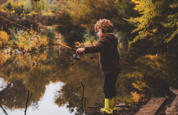 Kid with fishing-rod. Child fishing at autumn lake.