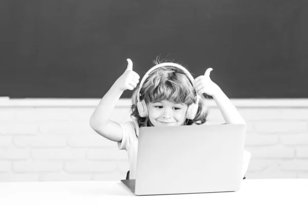 Skolbarn med tummen upp med bärbar dator och hörlurar i skolan. — Stockfoto