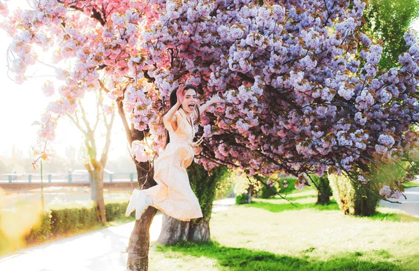 Rolig flicka hoppar i rosa körsbär blomma park. Semester med flicka i Sakura. Flicka och Sakura. Vacker ung kvinna njuter av solig dag i parken under körsbärsblom säsongen på en trevlig vårdag. — Stockfoto