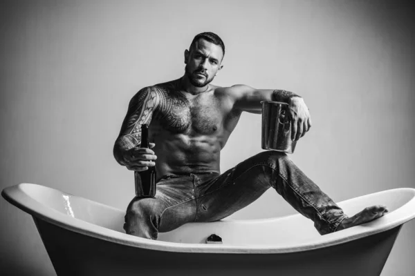 Sexy homme musclé séduisant assis sur la baignoire, les hommes vacances avec du champagne. Célébrer Noël ou anniversaire. Partie de sexe privé. — Photo