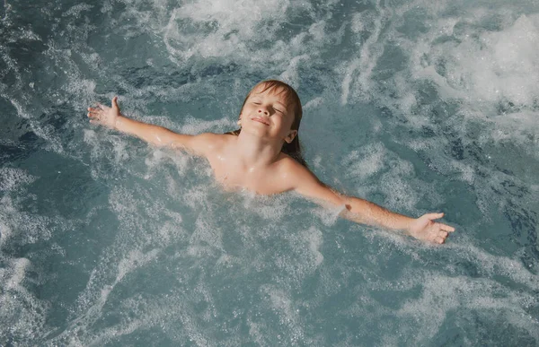 Verbazingwekkend kind spelen en spetteren in de zee. Dat joch heeft plezier buiten. Zomervakantie en gezond familie levensstijl concept. Kleine jongen heft handen omhoog in het water en spat water druppels. — Stockfoto