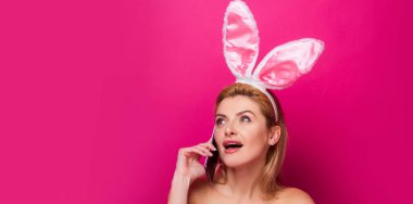 Tavşanlı Paskalya bayrağı. Paskalya tavşanı. Pembe arka planda izole edilmiş cep telefonlu genç bir kadın..