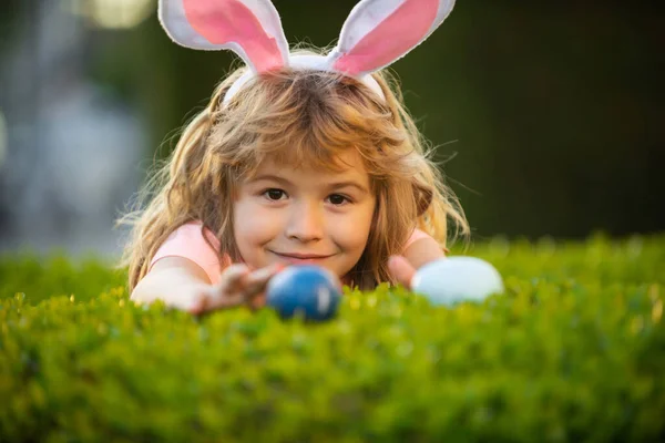 Paskalya yumurtası avlayan çocuklar. Tavşan kulaklı çocuk Paskalya yumurtası avında bahçede. — Stok fotoğraf