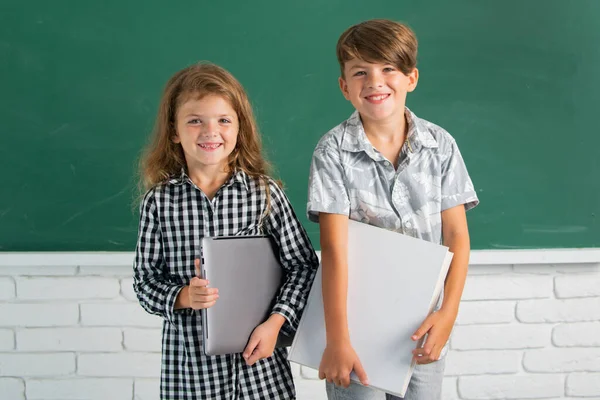 School children siblings hold book with surprising expression against blackboard. School kids friends. — Stock Photo, Image