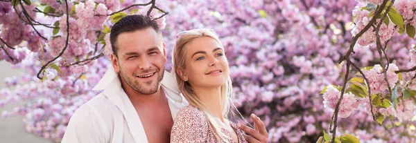 Coppia primaverile innamorata, striscione. Gli amanti hanno momenti romantici. Coppia sensuale donna e uomo in fiori rosa nel parco dei fiori estivi. — Foto Stock