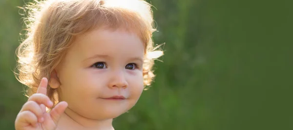 Banner tavaszi gyerek arccal. Közelkép portré egy aranyos baba zöld természet park napsütéses napon. A gyermekkor és a nevelés fogalma. — Stock Fotó