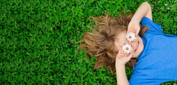 Banner met lentekind gezicht. Gelukkig kind liggend op groen gras in het voorjaarspark. Kinderen op groen gras achtergrond. — Stockfoto