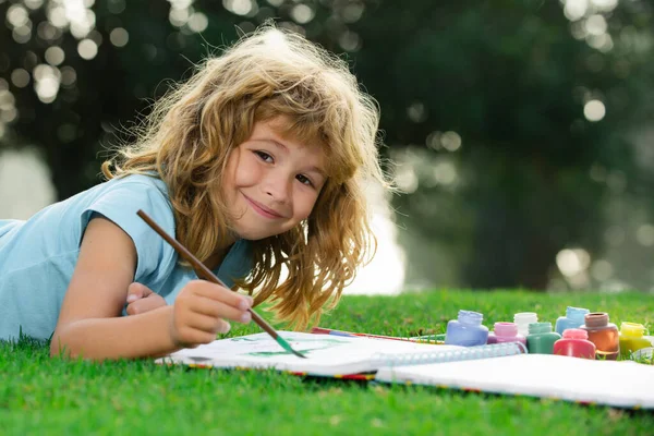 Kids drawing. Child boy draws in park laying in grass having fun on nature background. Kids artist creativity. Royalty Free Stock Images