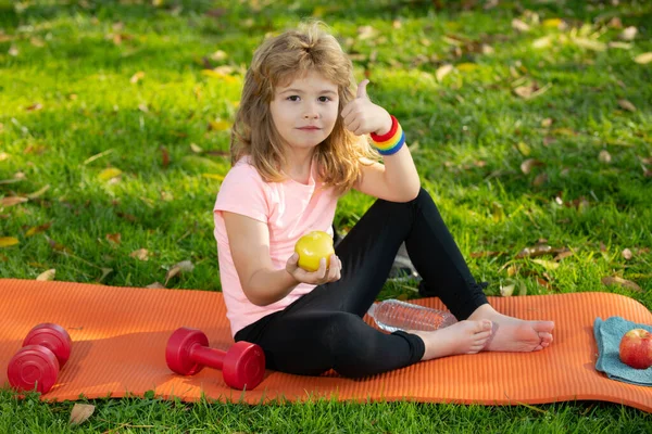 Hälsosam livsstil och hälsosam mat koncept. Liten pojke barn i sportkläder äta äpple sitter på idrottsmatta efter träning på solig vårdag. — Stockfoto