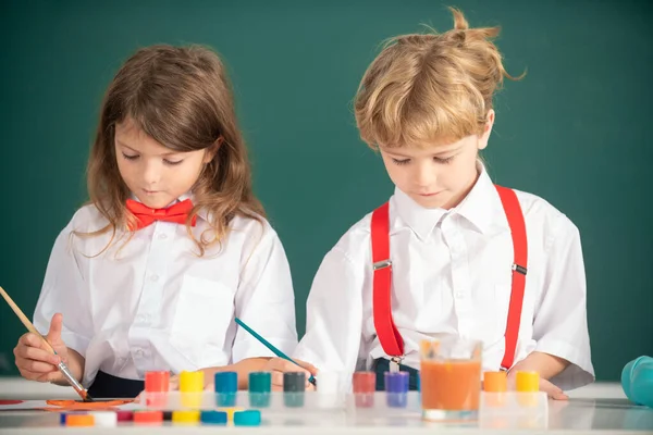 Escola crianças menina e menino pintura com tintas cor e escova em sala de aula. — Fotografia de Stock