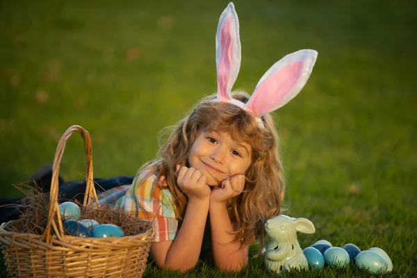 Chłopiec polujący na wielkanocne jajka, leżący na trawie. Wielkanocne króliczki. Królicze dzieci z króliczymi uszami. — Zdjęcie stockowe