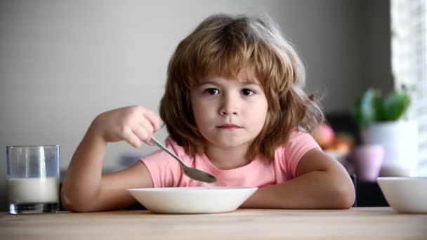 Dzieci jedzą owsiankę i mleko na śniadanie. słodkie chłopiec jedzenie zdrowe jedzenie z łyżka w domu. — Wideo stockowe